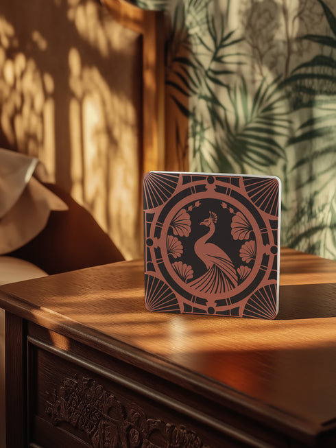 Square ceramic coaster featuring a detailed Art Deco peacock design in copper tones, surrounded by shell motifs and geometric fan patterns on a dark charcoal background, with protective cork base.